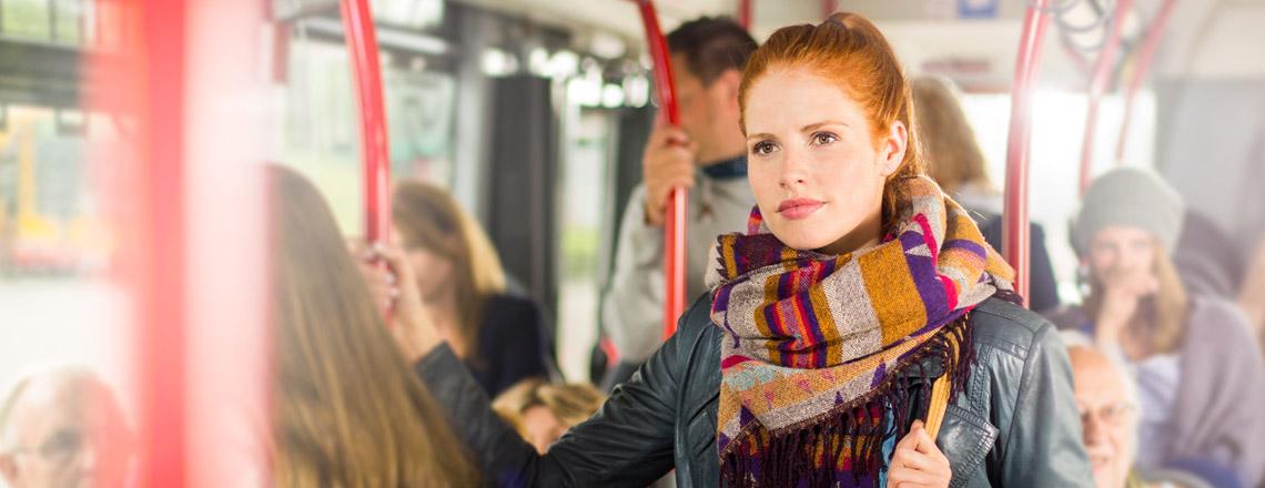 Erkältungsviren haften häufig an Haltestangen: Rothaarige Frau im Bus.