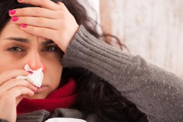 Eine Frau mit Grippe liegt im Bett und putzt sich die Nase