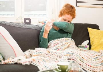 Aufgrund von Schnupfen muss eine Frau niesen.