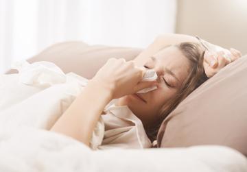 Frau mit Sinusitis im Bett überlegt, wann er zum Arzt gehen soll.
