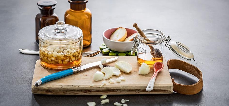 Auf einem Tisch liegen verschiedene Hausmittel gegen Halsschmerzen; beispielsweise Honig und Knoblauch
