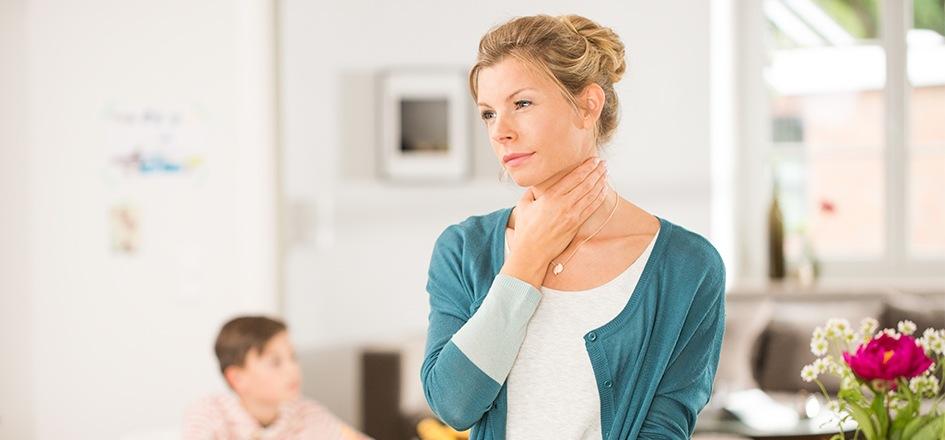Eine Frau hält sich die Hand an den Hals, weil sie Schluckbeschwerden hat.