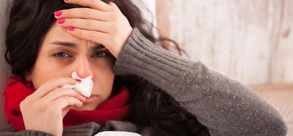 Eine Frau mit Grippe liegt im Bett und putzt sich die Nase