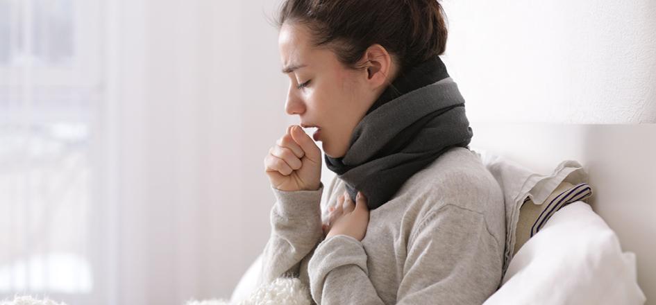 Frau mit Bronchitis-Symptomen sitzt krank auf dem Sofa.